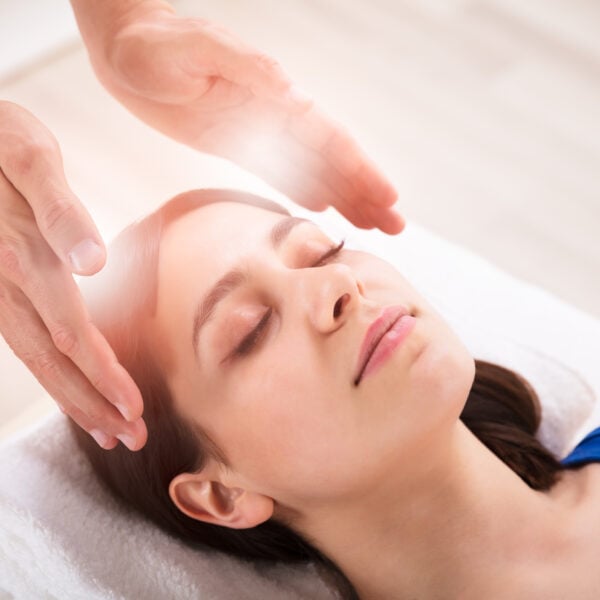 Close-up Of Therapist's Hand Performing Reiki Treatment On Young Woman In Spa